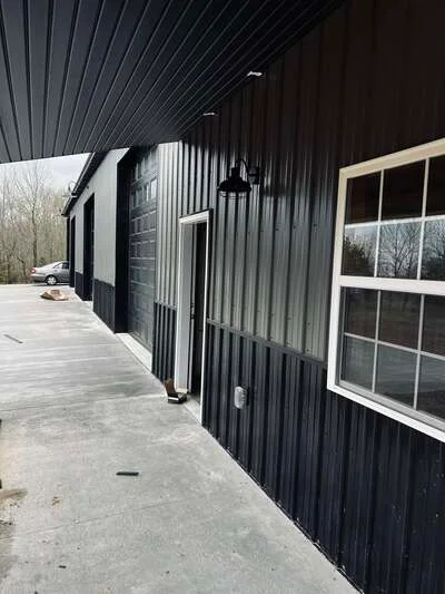 Finished concrete pad and walkway beside black metal building with white-trimmed windows