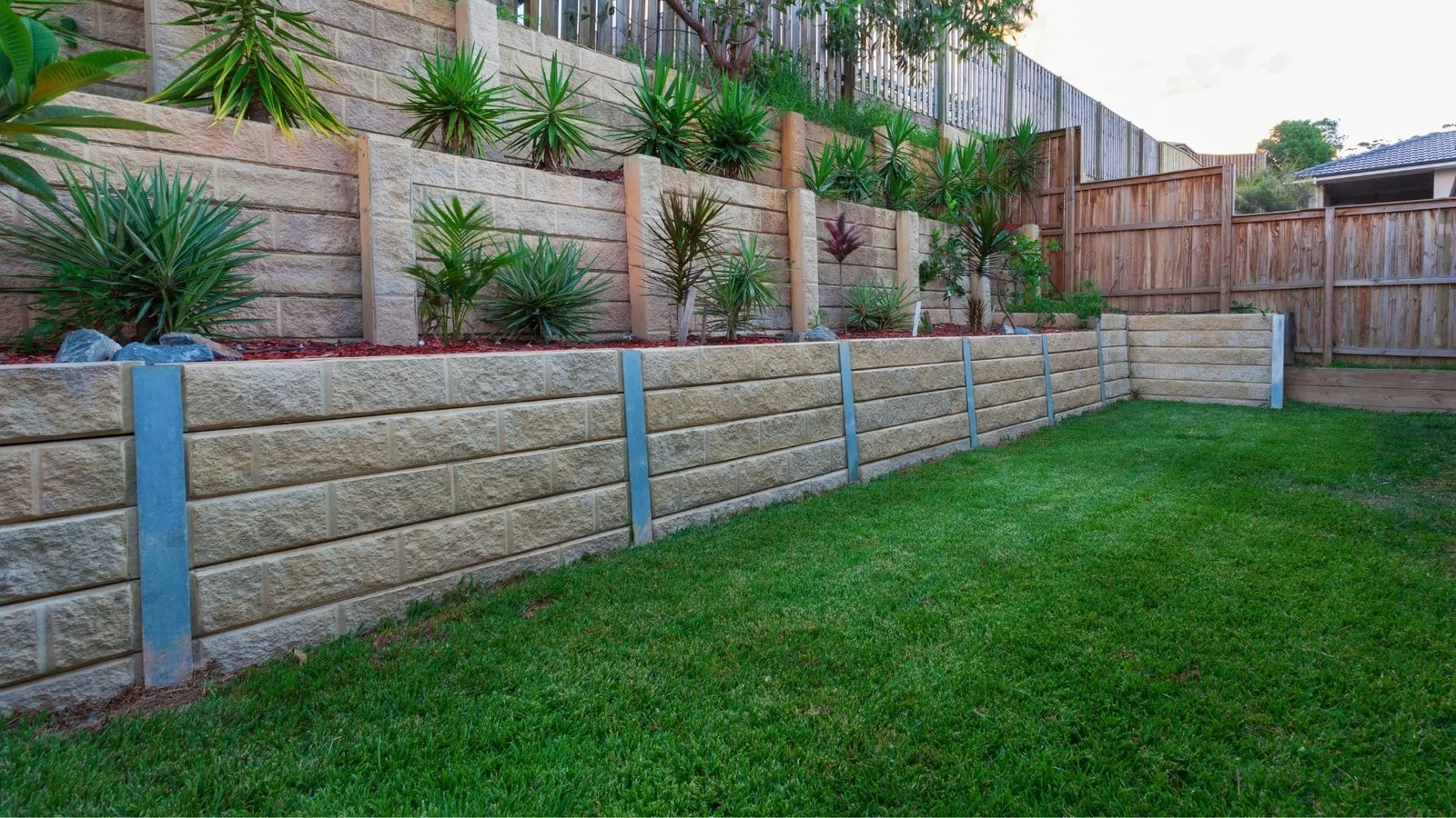 Textured concrete block retaining wall with steel posts and landscaping above