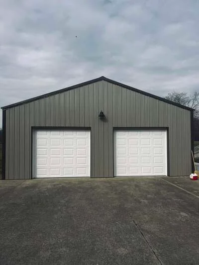 Concrete apron in front of two-bay metal garage with white overhead doors