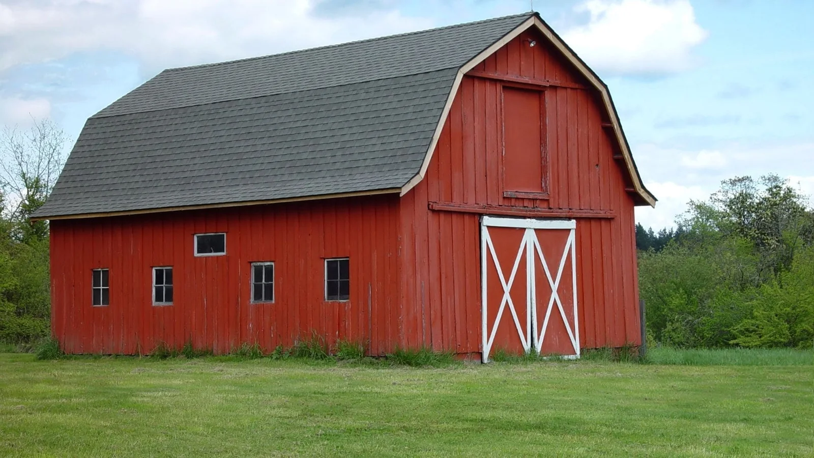 Red barn with white X-pattern doors on concrete foundation and gray shingled gambrel roof