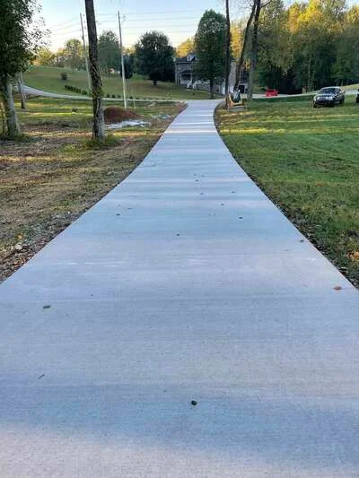 Curved concrete walkway with smooth finish, winding through landscaped yard with trees