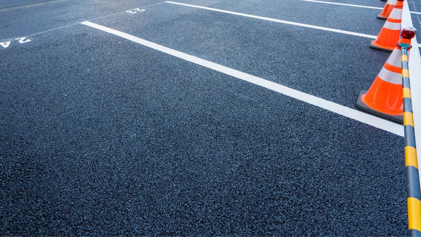 Newly paved asphalt lot with white lane lines, directional arrows, and orange traffic cones