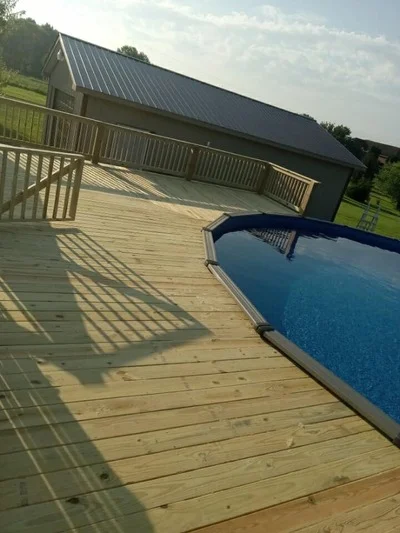 Wooden deck with railings adjacent to in-ground pool and residential home