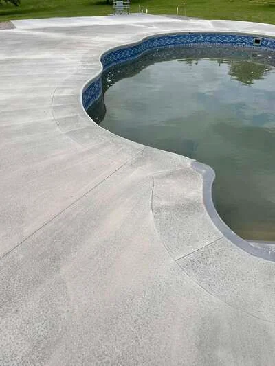Stamped concrete pool deck with curved edges and broom finish texture surrounding in-ground pool