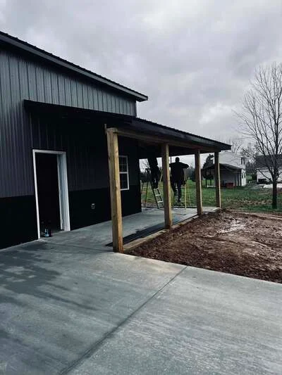 Concrete apron and pad with wooden post-frame porch attached to metal agricultural building