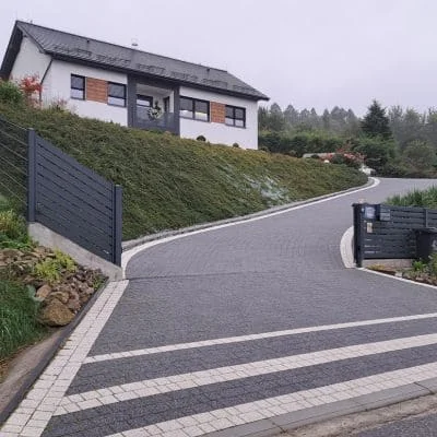 Curved concrete driveway with gray and white striped pattern, decorative edging, and modern home